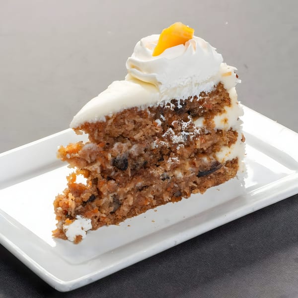 A slice of carrot cake with white frosting and a candied orange peel on a white plate.